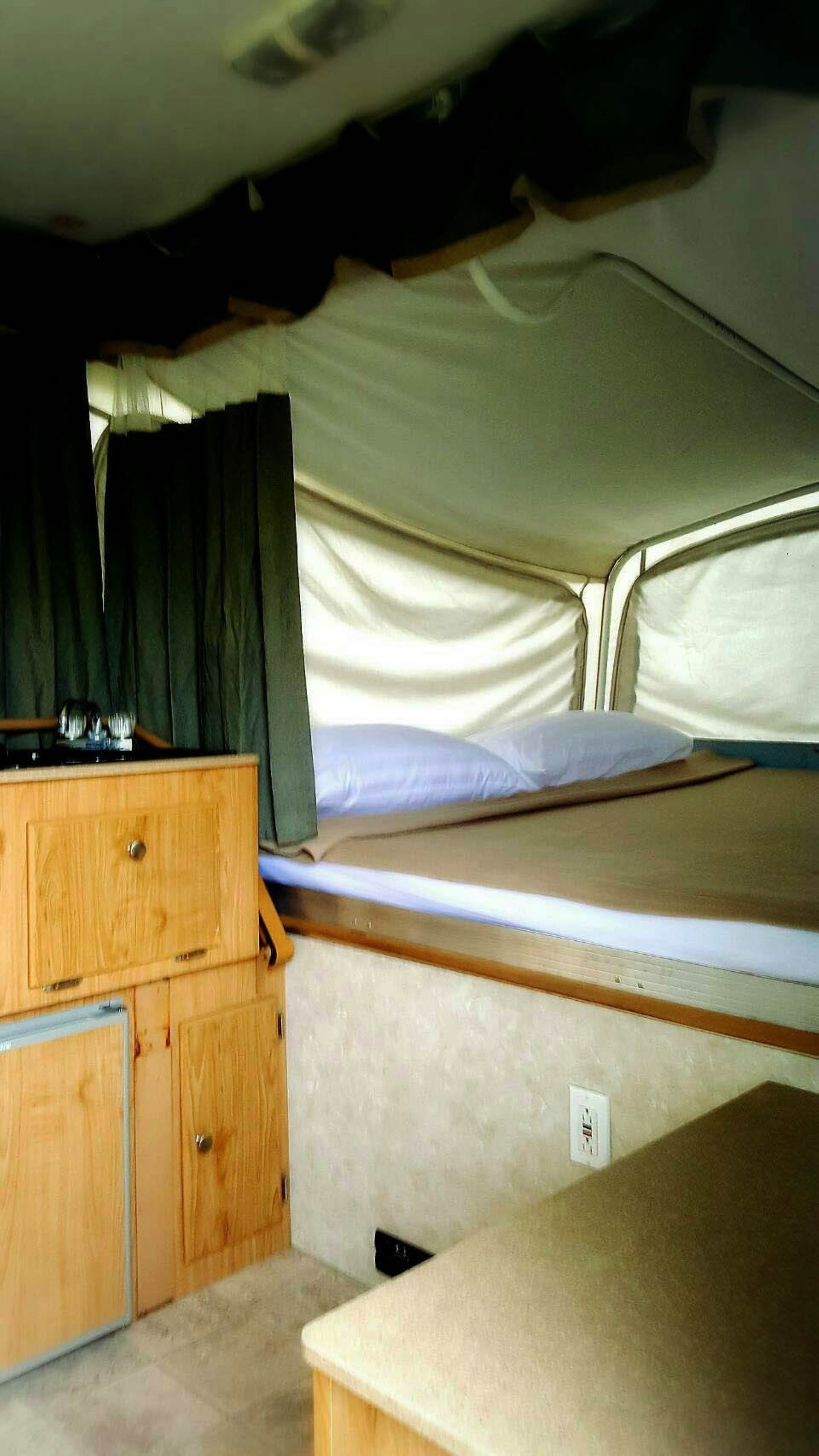 Interior compacto de autocaravana con cama, cómoda de madera y pequeña zona de kitchenette.