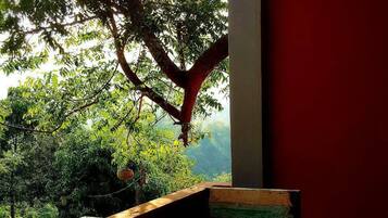 Una mesa y sillas de madera en un patio con baldosas, con vistas a zonas verdes y un edificio al fondo.