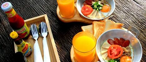 Bandeja de desayuno con tostadas, un plato de huevos y un vaso de jugo de naranja sobre una mesa de madera.