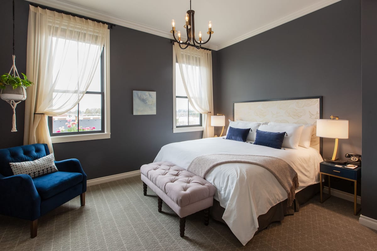 A bedroom with a large bed, two bedside tables, a blue armchair, and a hanging plant.
