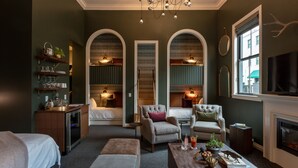 A hotel room with a fireplace, a television, a coffee table with decorative items, and a seating area with two armchairs and a sofa. - Atticus Hotel (McMinnville)