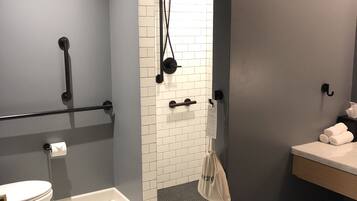 A bathroom with a toilet, a shower with a white tiled wall, and a sink with a towel rack.
