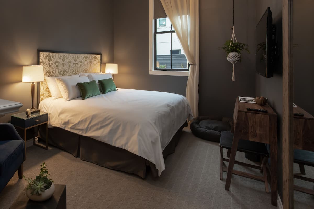 A bedroom with a large bed, bedside tables, a desk, a chair, and a window with curtains.