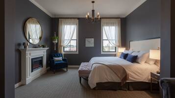 Een slaapkamer met een groot bed, een open haard, een blauwe fauteuil en een kroonluchter.