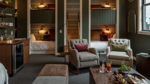 A cozy hotel room with a seating area, a minibar, and a view of the city.