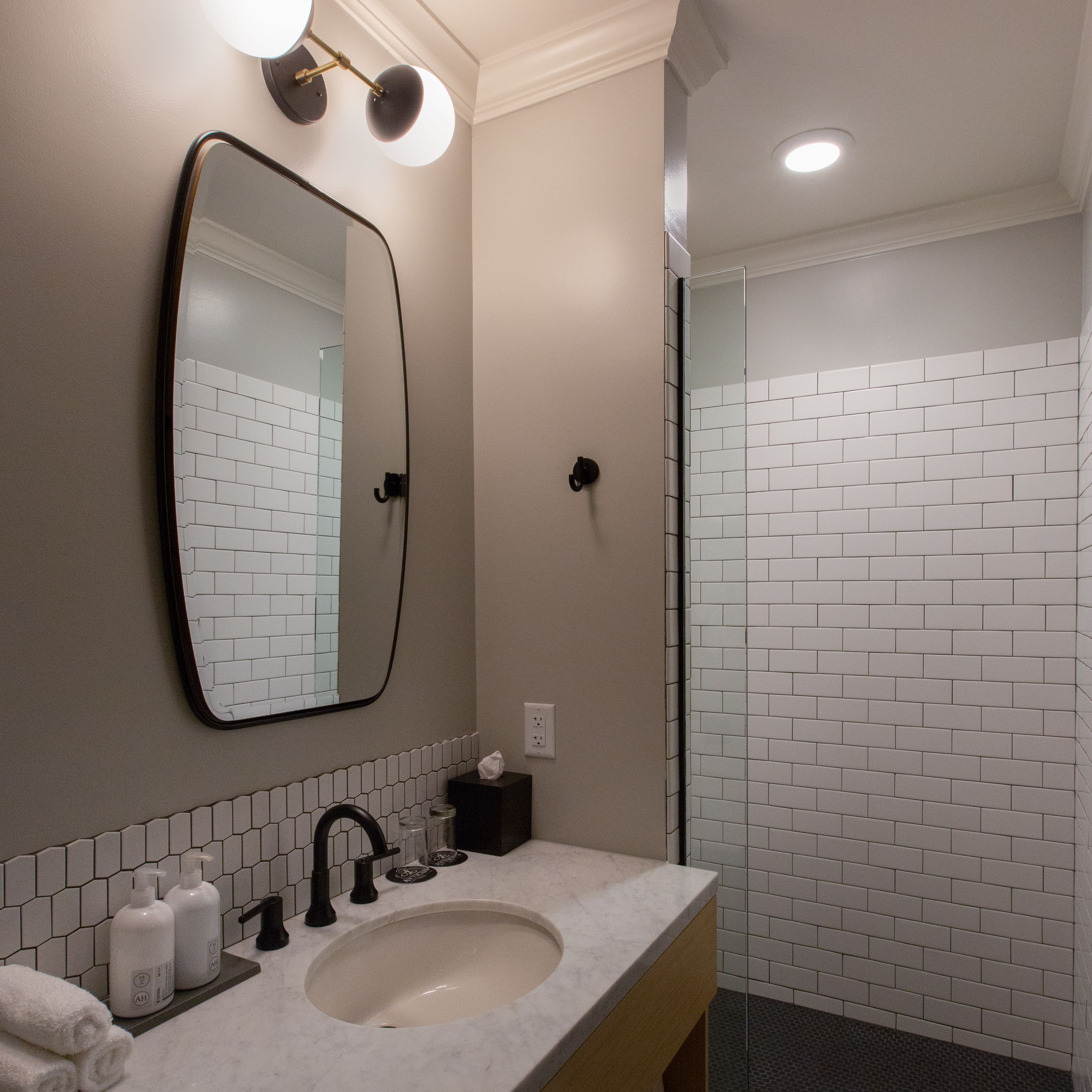 A bathroom with a sink, mirror, and white tiled shower.