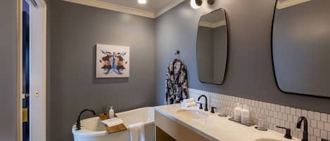 Une salle de bain moderne avec une baignoire sur pieds, un grand miroir et un lavabo double.