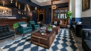 A modern living room with a dark blue wall, green armchairs, a wooden coffee table, and a patterned rug.