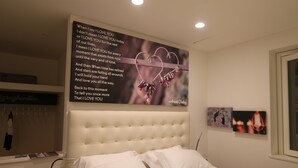 Un dormitorio con una cama grande, un cabecero, una mesita de noche con lámpara y una pared con un cartel.