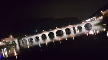 Une vue nocturne d’un pont à arches multiples enjambant une étendue d’eau, illuminé par des lampadaires.