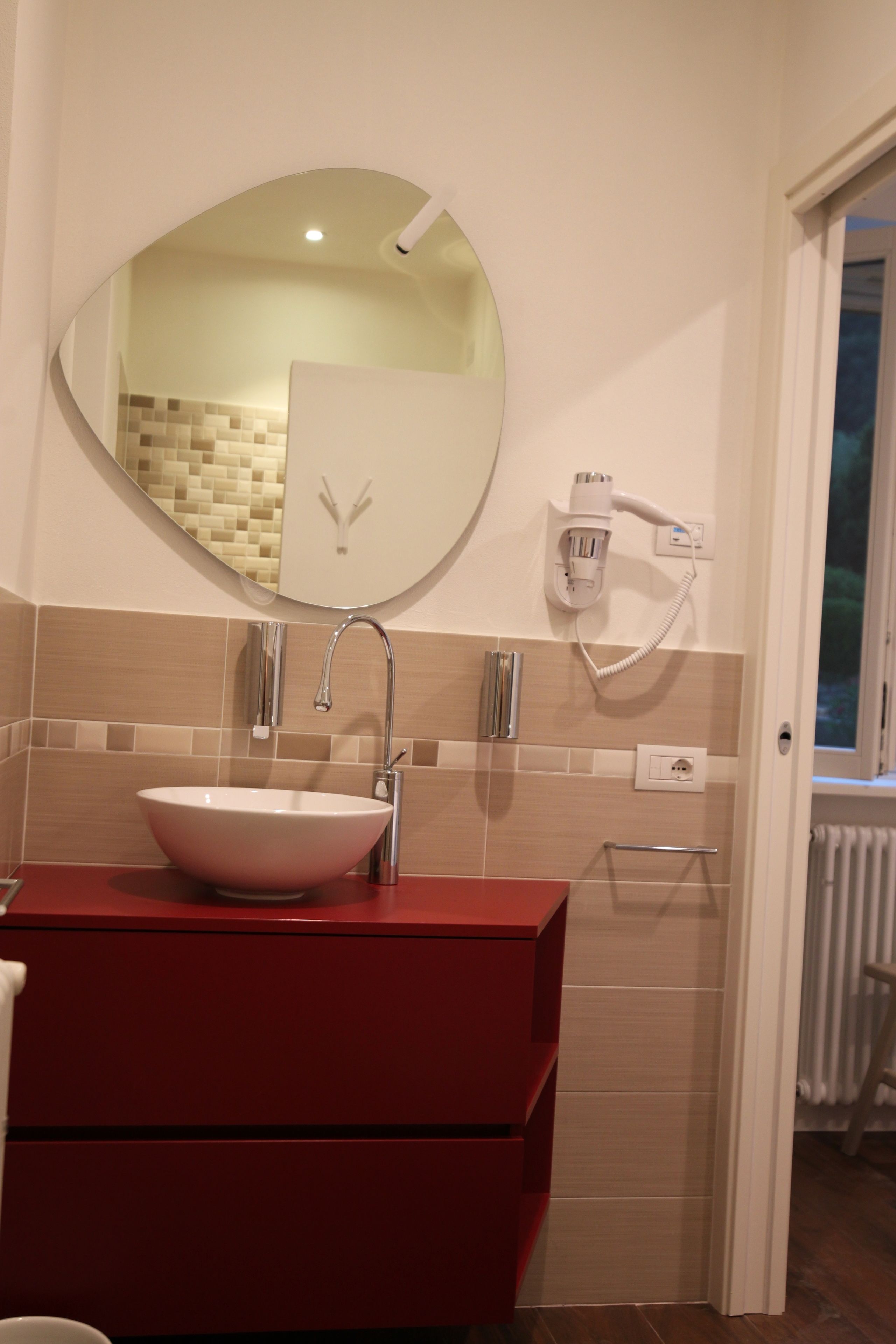 A bathroom with a round mirror, a white sink, and a red vanity.