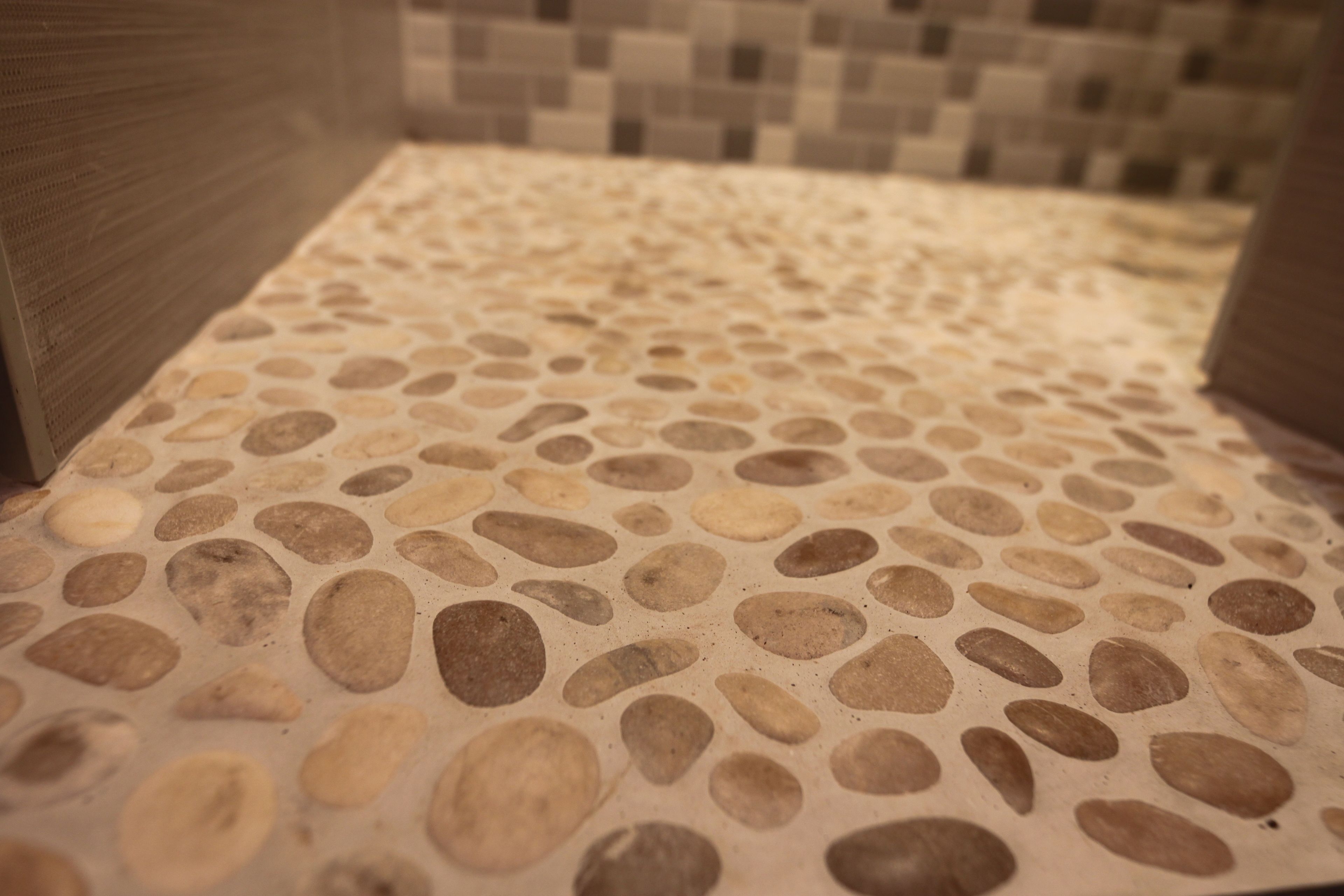 Ein Badezimmer mit Kieselsteintapete am Boden und einer Wand aus Mosaikfliesen.