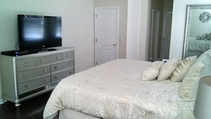 A bedroom with a bed, dresser, television, and a door.