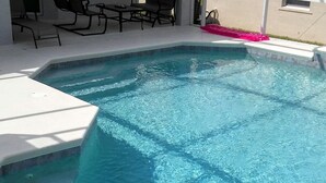 Una piscina con bordo piastrellato, circondata da un portico coperto con sedie e un tavolo.