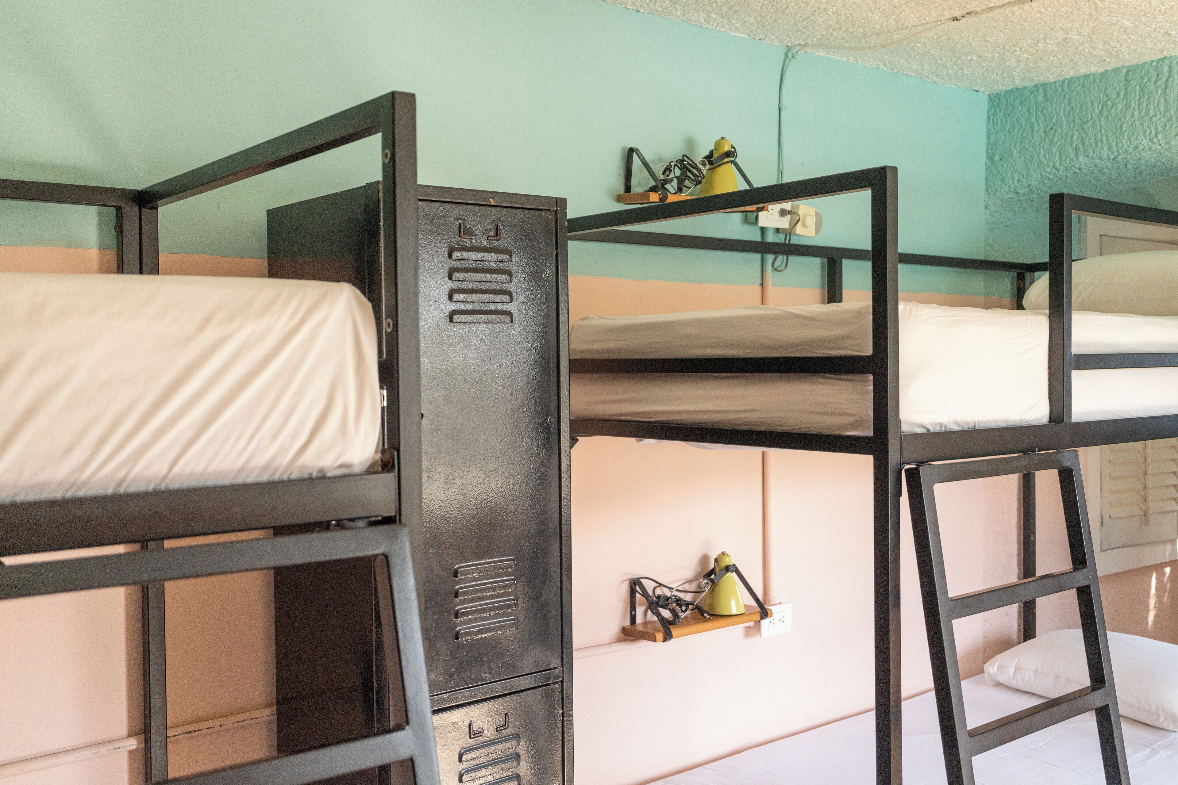 A bunk bed room with a metal bunk bed structure, a shelf with a lamp, and a power outlet on the wall.