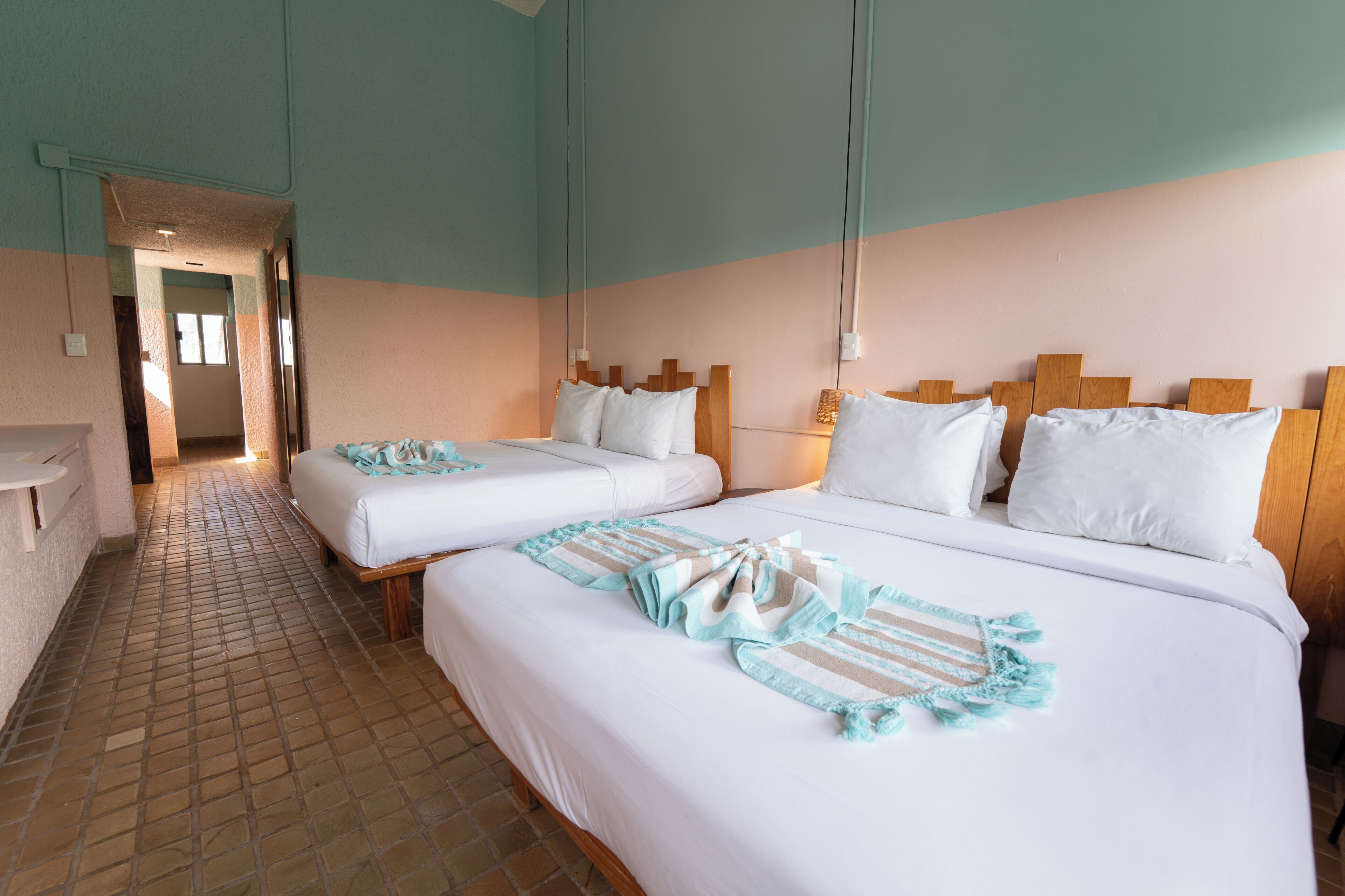 A hotel room with two beds, a tiled floor, and a hallway leading to another room.