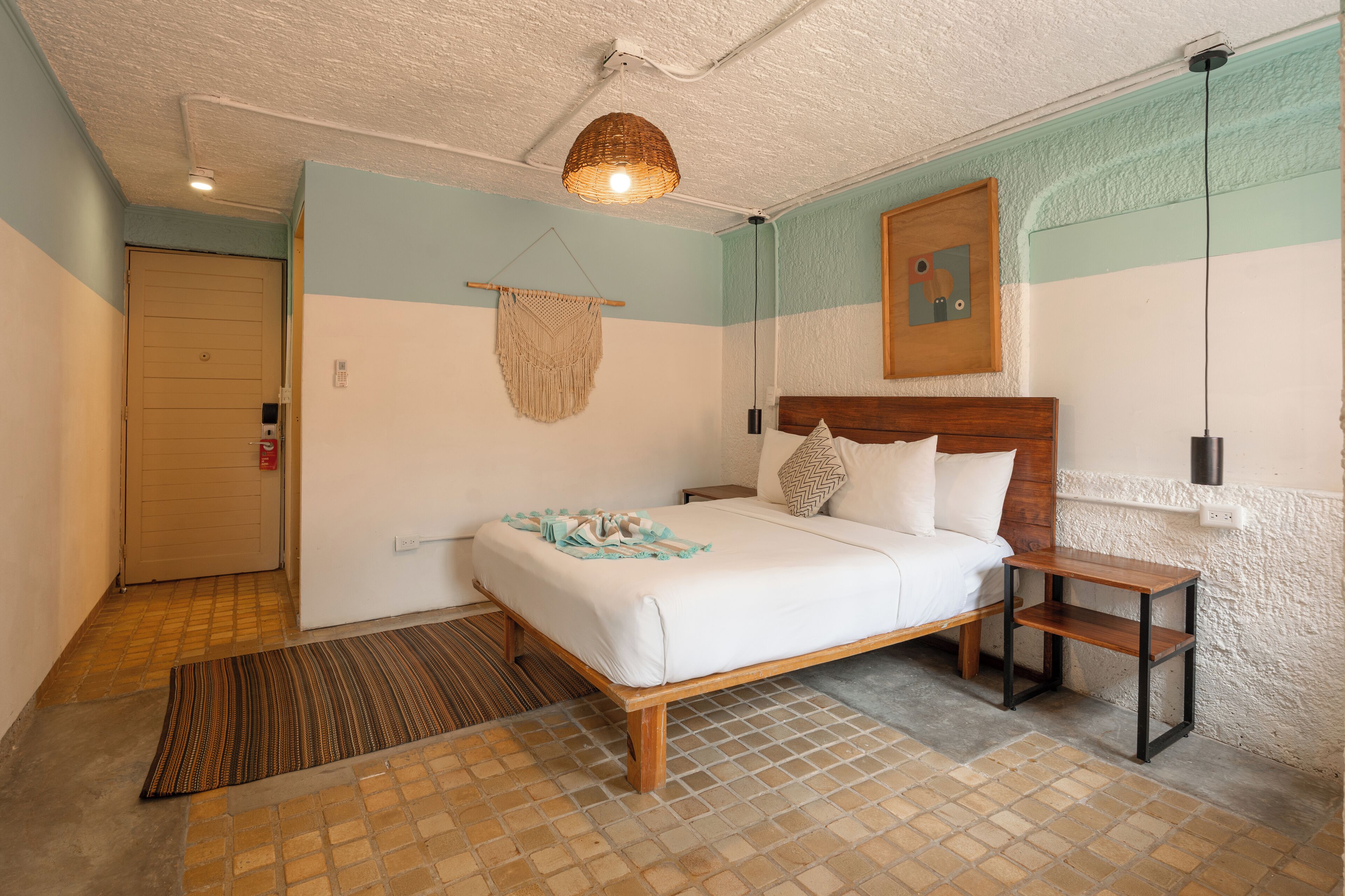 Une chambre à coucher avec un lit, une table de chevet, une décoration murale en macramé, une tête de lit en bois et un tapis à motifs.