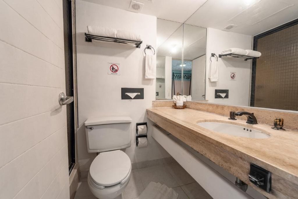 A modern bathroom with a toilet, two sinks, a large mirror, and a towel rack.