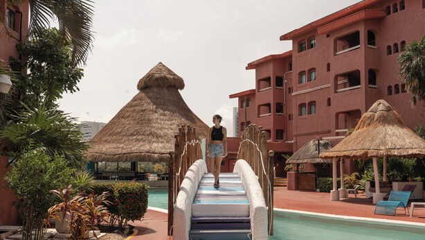 Un espace piscine agrémenté d’un pont à toit de chaume menant à un coin salon situé au bord de la piscine.