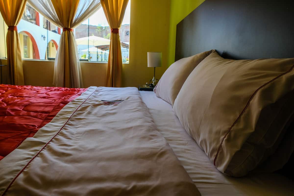 Habitación de hotel con cama, cortinas, lámpara y vistas al exterior.