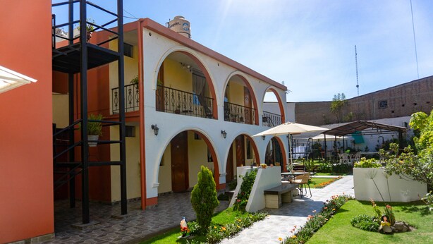 A courtyard with a two-story building featuring arched balconies, outdoor seating, and a garden with flowers. - Casa Baraquel (Arequipa)