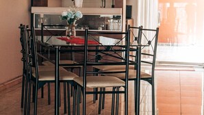 A dining area with a table and chairs, a vase with flowers, and a kitchen in the background. - Casa Baraquel (Arequipa)
