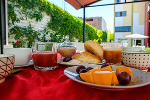 A breakfast table with a red tablecloth, a glass of tea, a glass of orange juice, a plate with bread, fruit, and a glass jar. - Casa Baraquel (Arequipa)