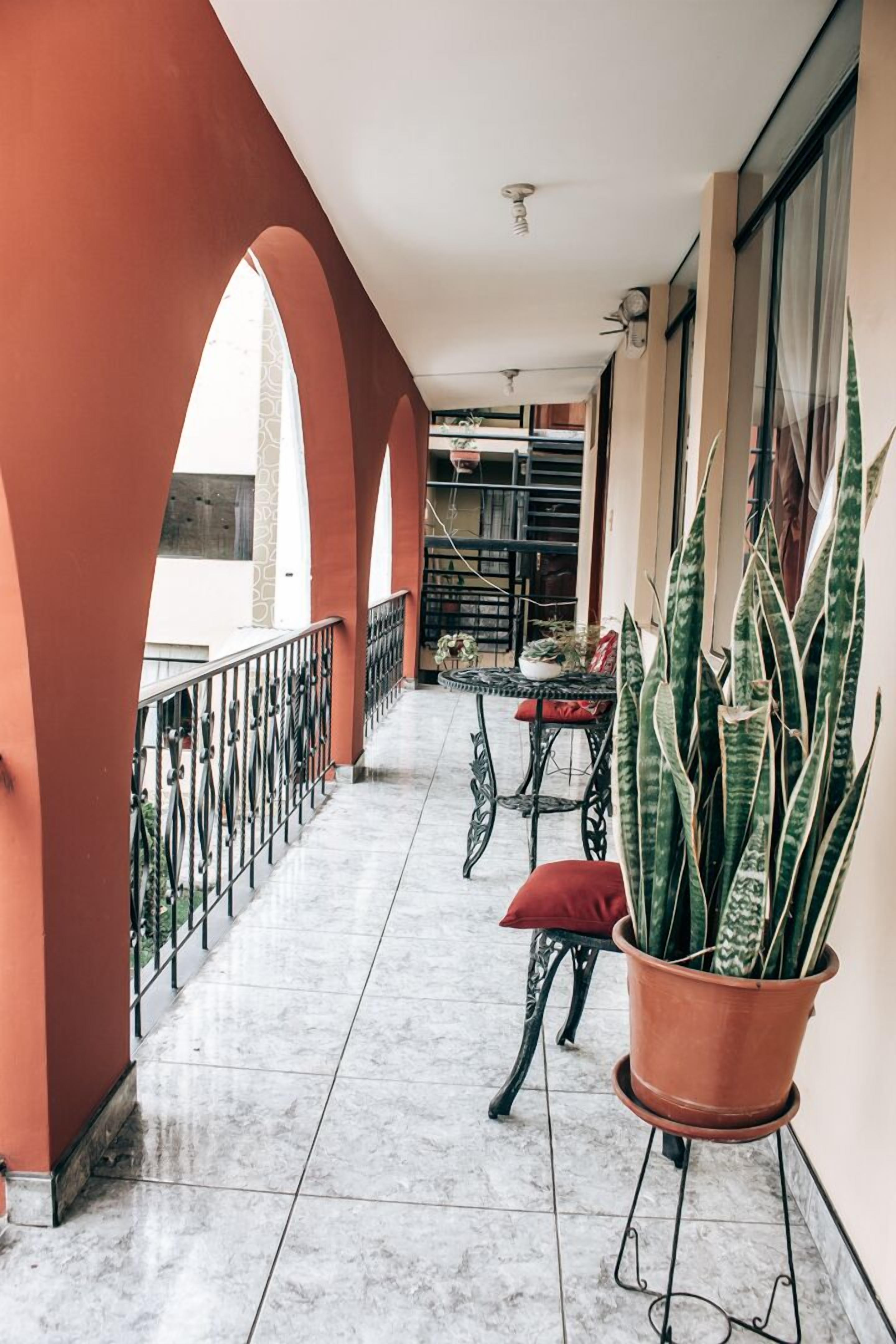 A covered balcony with a tiled floor, a table with chairs, and potted plants.