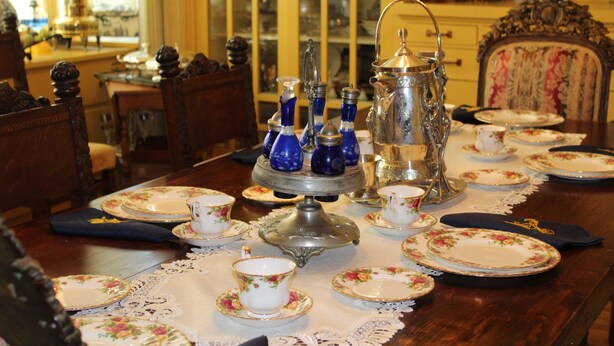 A dining table set with floral-patterned plates, cups, and a silver tea service. - Amie St.Jéan Bed and Breakfast (Rapid City)