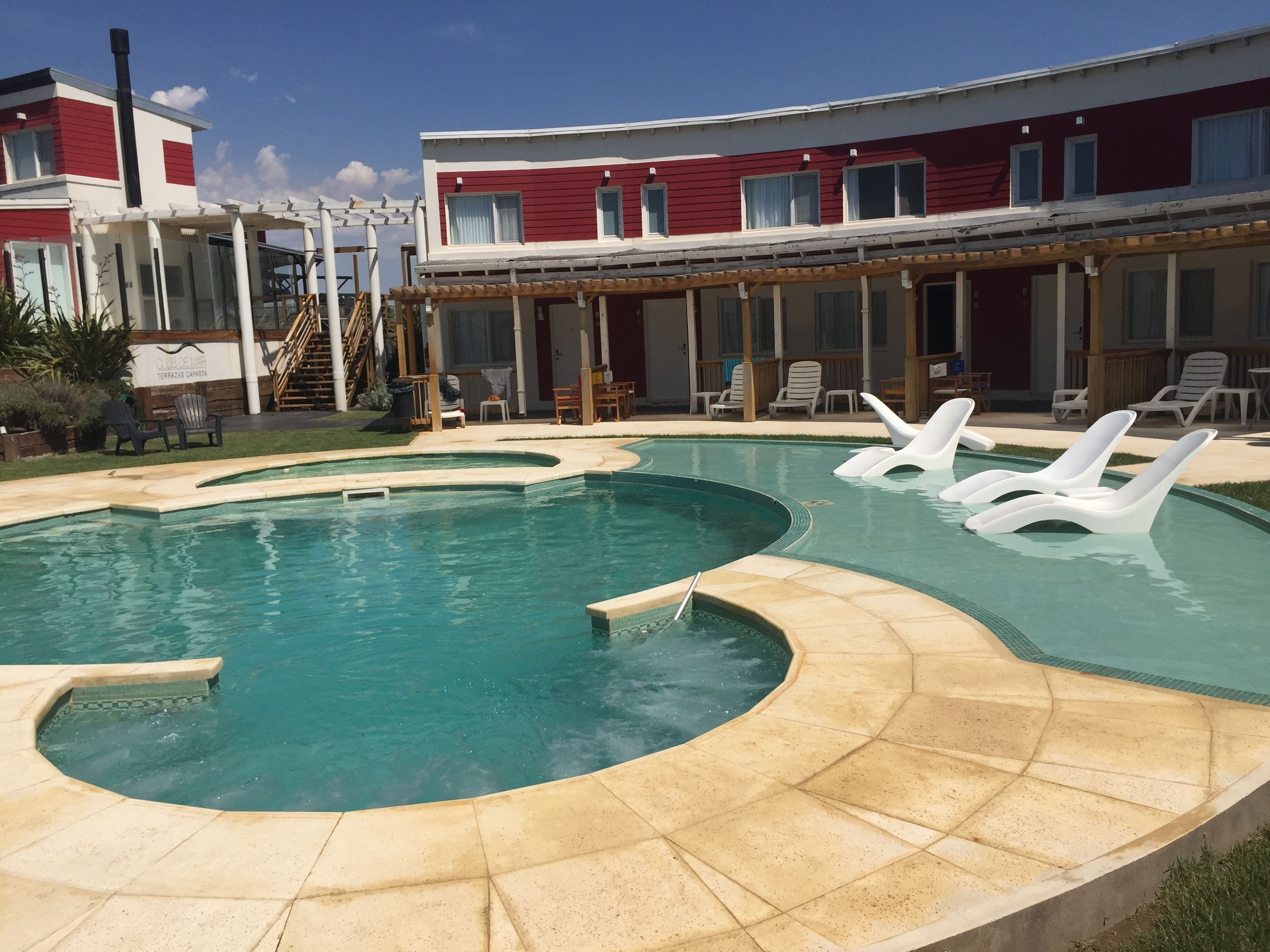 Una piscina con sillas de descanso y un edificio con paredes exteriores rojas y blancas.