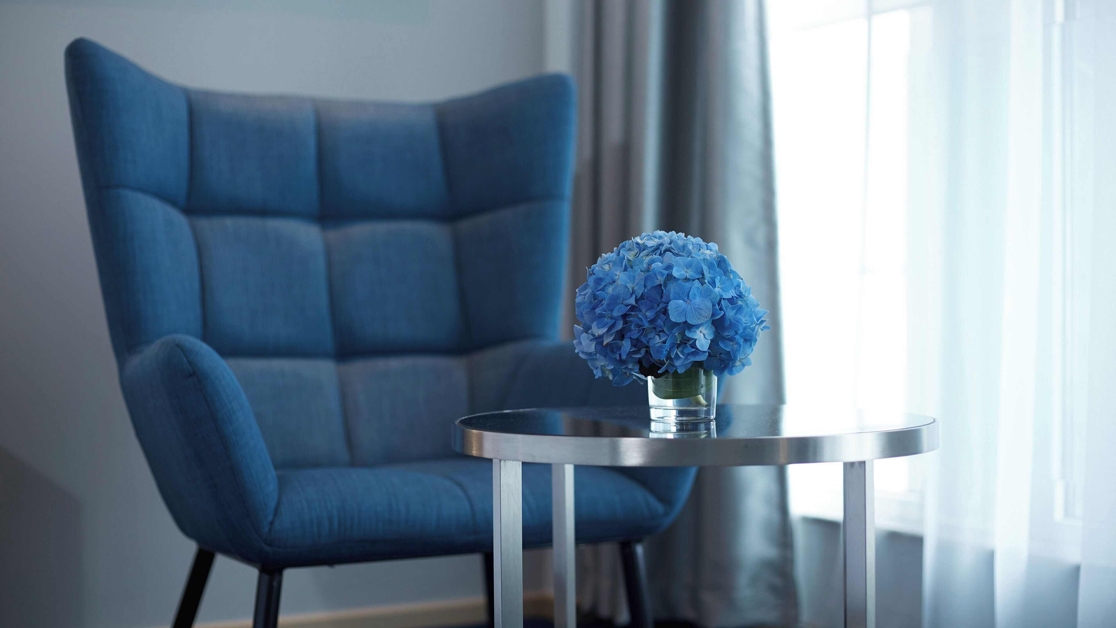 A modern room with a blue armchair and a round table with a vase of blue flowers.
