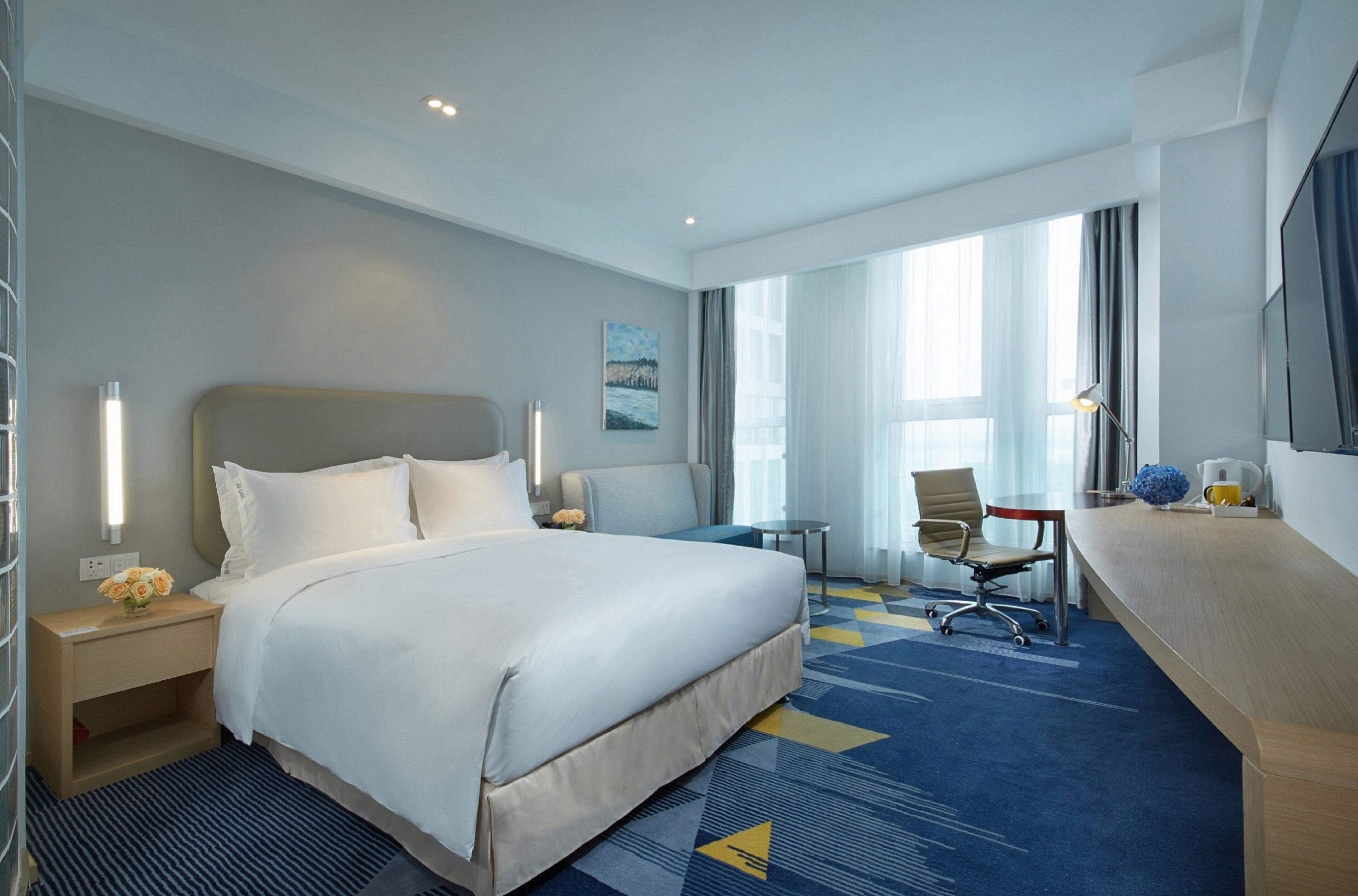 A hotel room with a large bed, a desk, a chair, and a TV.