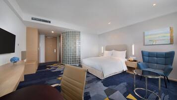 A hotel room with a bed, a desk, a chair, a TV, and a painting on the wall.