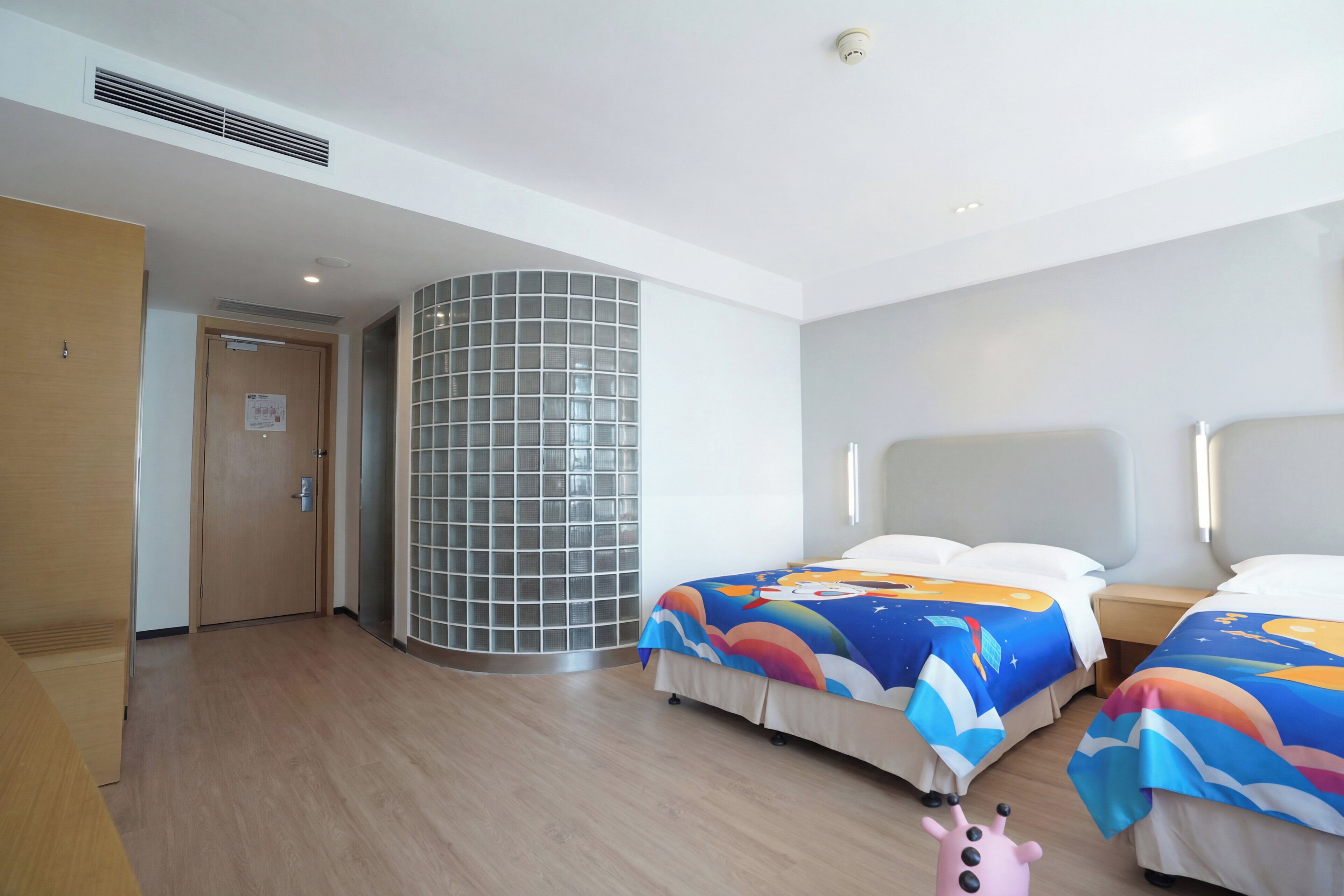 Habitación de hotel con dos camas, una puerta de madera, una división de vidrio y un respiradero en el techo.