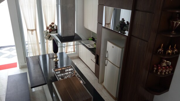 A modern kitchen with a central island, a built-in oven, and a large window with curtains. - T-Rooms Homestay (Palembang)