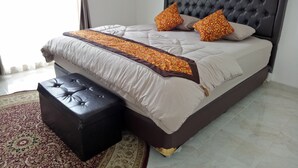 A neatly made bed with a dark headboard, two decorative pillows, a brown throw blanket, and a matching ottoman. - T-Rooms Homestay (Palembang)
