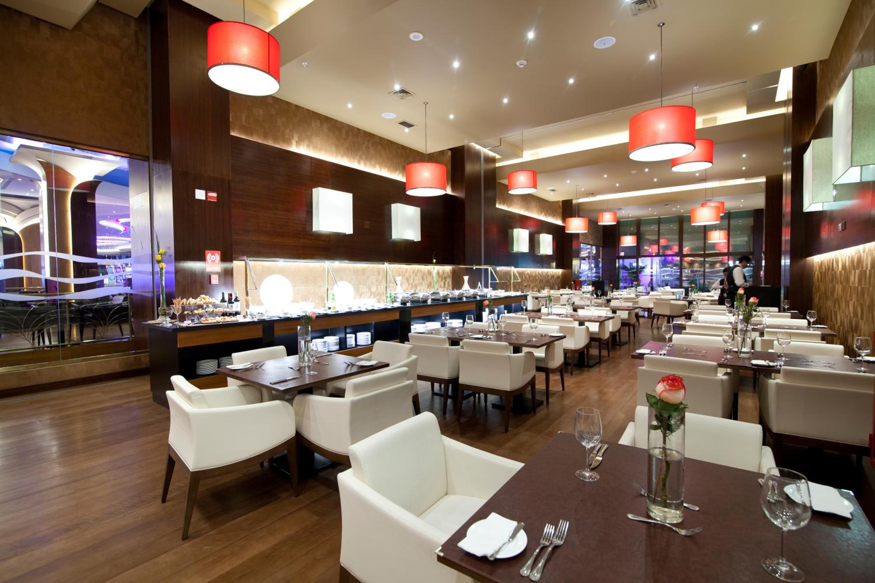Restaurante moderno com várias mesas de jantar, cadeiras brancas e iluminação pendente vermelha.