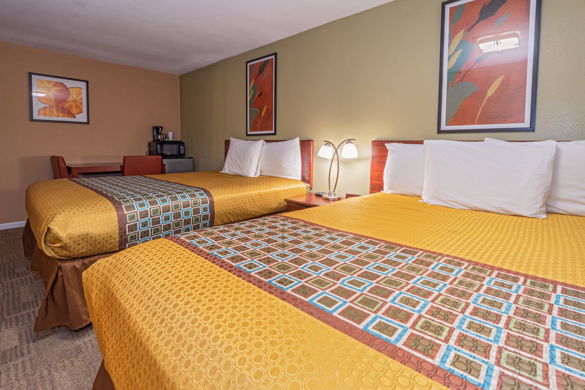 A hotel room with two beds, a desk, a chair, a microwave, and a coffee maker.