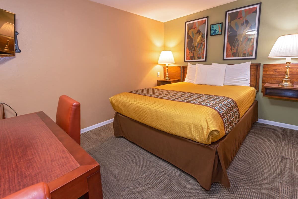A hotel room with a bed, a desk, and a chair. There are two wall-mounted lamps and framed artwork above the bed.