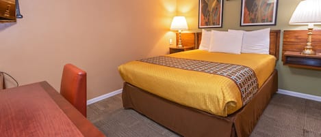 Habitación de hotel con cama, escritorio y silla. Dos lámparas de pared y cuadros decoran la pared sobre la cama.