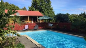 Una piscina con sillas de descanso y una terraza de madera, rodeada de vegetación.