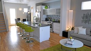 Una cocina moderna con una isla central, taburetes de bar y un comedor con sillas.