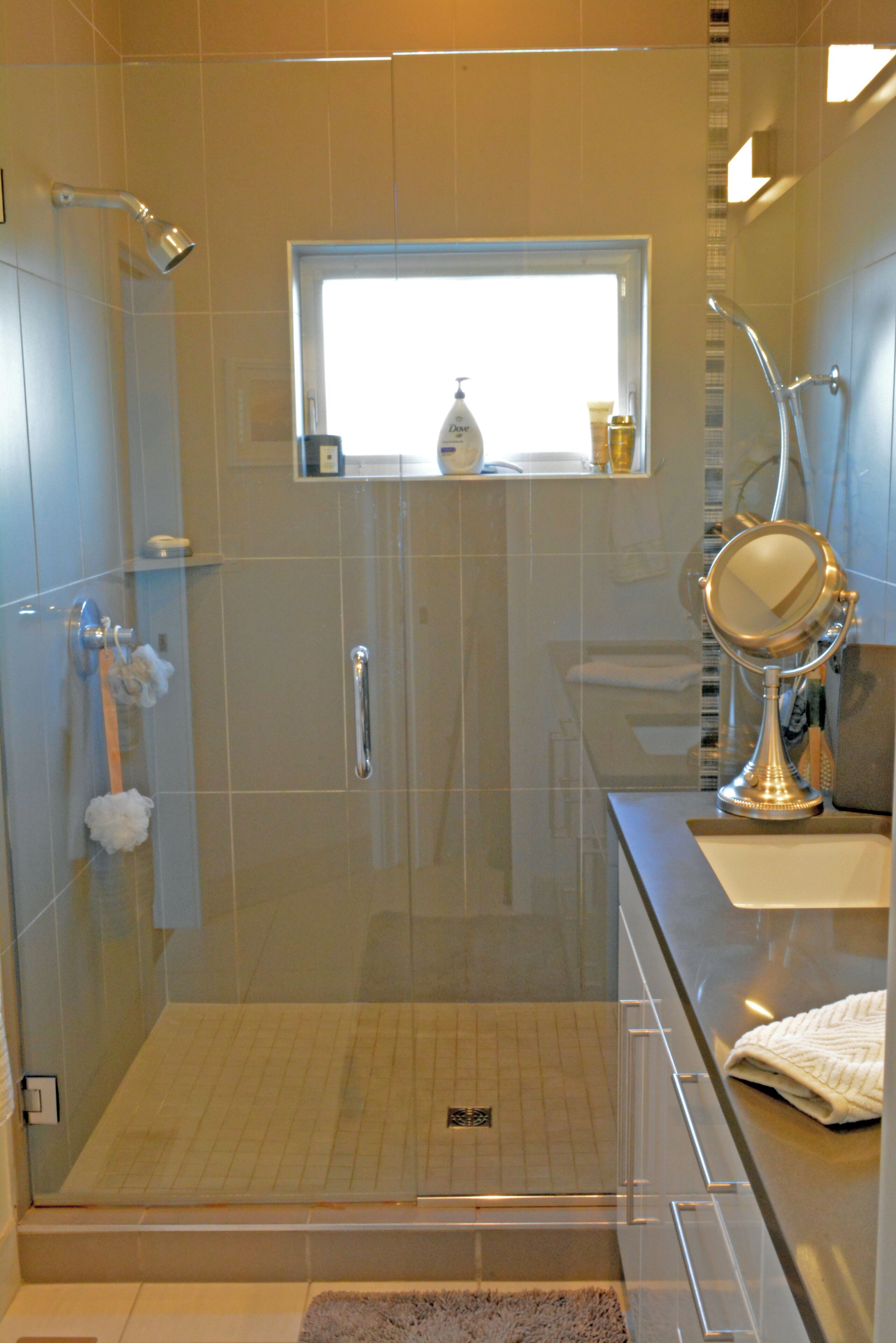 A modern bathroom with a glass-enclosed shower, a vanity with a mirror, and a window above the sink.