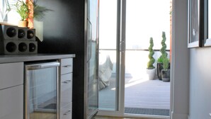 Cocina moderna con refrigerador, lavamanos y ventana. Se ve una puerta que da a un balcón con plantas en macetas.