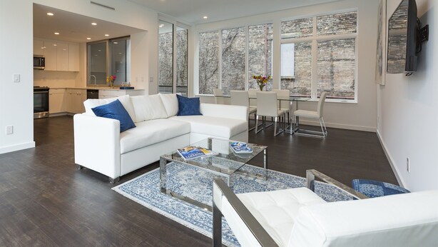 A modern living room with a white sofa, a glass coffee table, and a dining area with a white table and chairs. - Unique, contemporary 1,500ft2 2BR/2.5BA apt - OTR (Cincinnati)