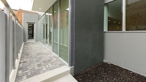 A corridor with glass doors, a brick pathway, and a building with a grey exterior. - Unique, contemporary 1,500ft2 2BR/2.5BA apt - OTR (Cincinnati)