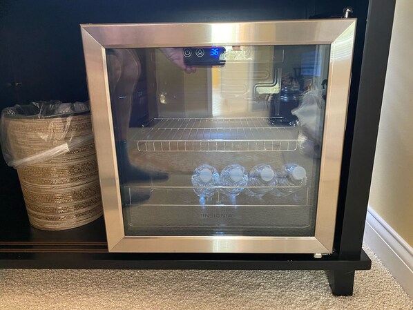 A framed microwave with a digital display, a basket of items, and a shelf with clear bottles.