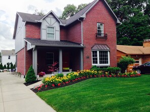 A two-story brick house with a front porch, a small garden with flowers, and a visible address number. - Butler Fieldhouse one block from Butler University and Hinkle Fieldhouse (Indianapolis)