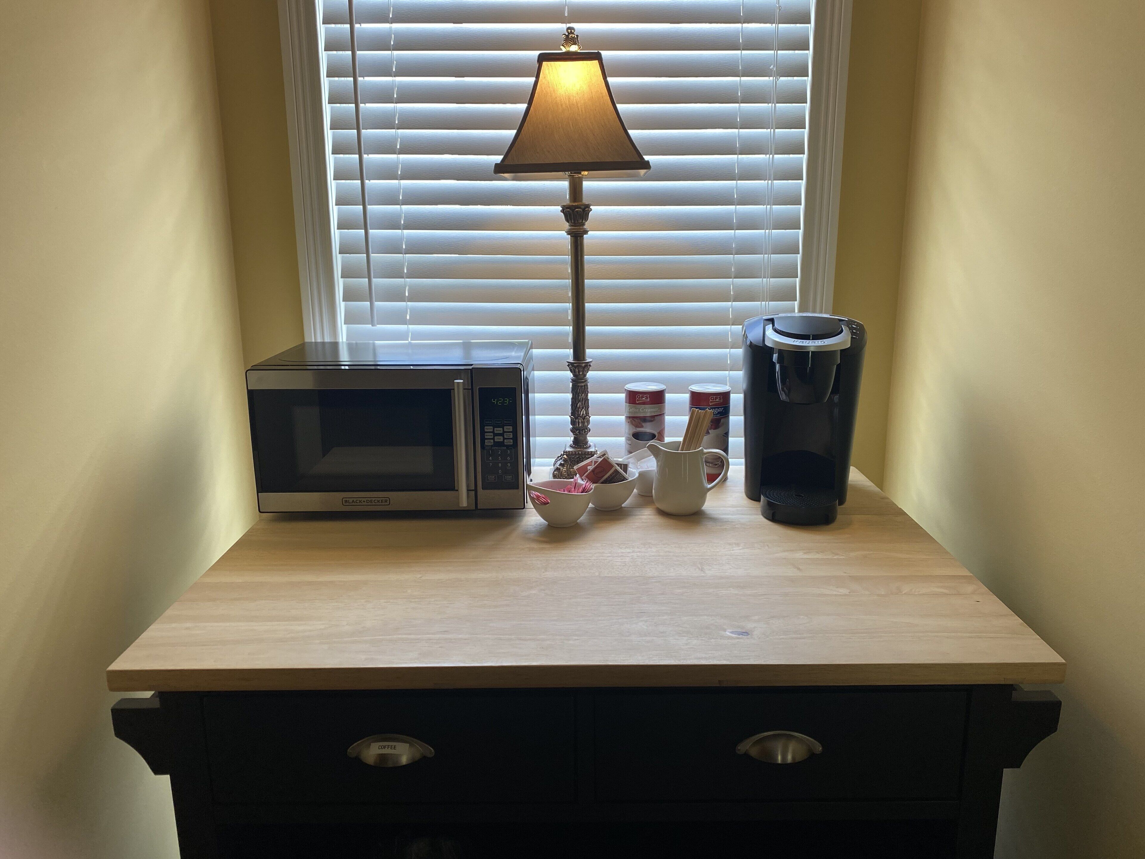 Een kitchenette met een magnetron, koffiezetapparaat en een lamp.