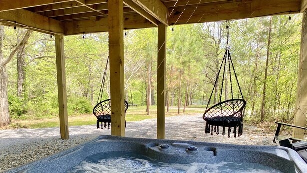 Ein Whirlpool unter einer Hollaube mit Hängestühlen, umgeben von Bäumen.